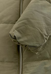 Olivovo zelená prešívaná bunda s lesklou textúrou, s celozipsovým uzáverom a zberanými rukávmi pre teplo.