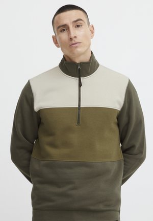 Zip-up fleece pullover in olive green, cream, and dark green; features color-blocking design, high collar, and textured fabric.