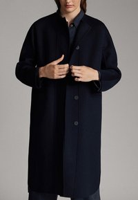 Cappotto di lana navy con taglio dritto, ampio rever e sei bottoni, dotato di due tasche laterali e finitura in tessuto texturizzato.