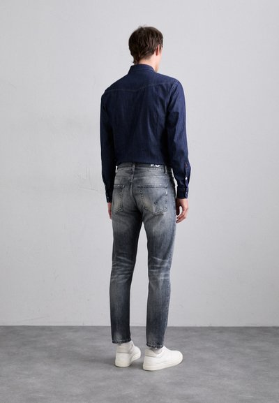 Camicia di denim navy, jeans grigi sfumati slim-fit e sneakers bianche. La camicia presenta un colletto a punta e polsini con bottoni.