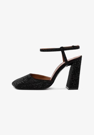 Scarpa nera con tacco alto e punta affusolata, decorata con borchie nere e una cinghia alla caviglia. Presenta un tacco grosso decorato e una morbida fodera interna.