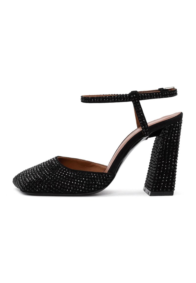 Scarpa nera con tacco alto e punta affusolata, decorata con borchie nere e una cinghia alla caviglia. Presenta un tacco grosso decorato e una morbida fodera interna.
