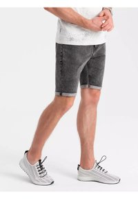 Shorts en denim gris avec ourlets retroussés, présentant une texture légèrement usée. Associés à des baskets en maille blanches avec des lacets et des accents noirs.