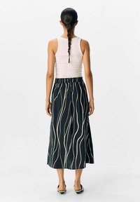 Jupe midi noire avec des lignes ondulées crème, ceinture froncée et tissu léger. Associée à un débardeur blanc et des sandales simples.