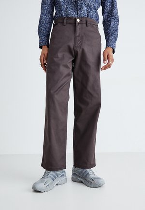 Brown wide-leg trousers made from cotton, featuring a front button closure and side pockets, paired with gray athletic shoes.