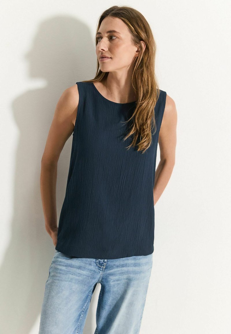 Débardeur bleu marine sans manches avec une finition texturée et un col rond, associé à un jean bleu clair. Design minimaliste avec une coupe décontractée.