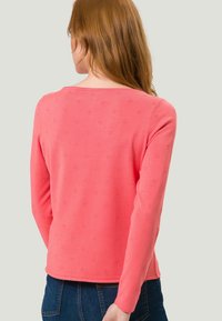 Suéter de manga larga color coral claro con cuello redondo, que presenta un patrón texturizado y un diseño ajustado. Tejido de punto suave.