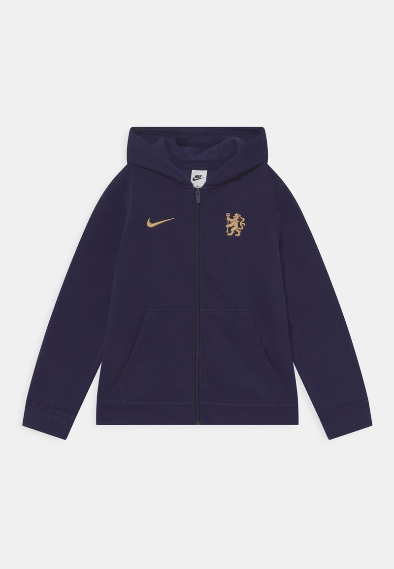 Sudadera con cremallera en color marino, hecha de tejido suave, con un logo dorado de Nike y un escudo. Las características destacadas incluyen un bolsillo tipo canguro y una capucha con cordón.