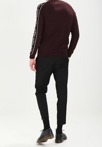 Burgundy sweater with patterned sleeves, paired with black tapered pants and black shoes. Smooth texture, crew neck design, minimal detailing.