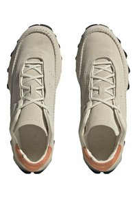 Ljusbeige mockaskor med svarta gummisulor, med snörningsdesign och en kontrasterande orange accent vid hälen.