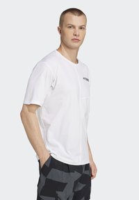 Hvid kortærmet t-shirt med rund hals, med en lille brystlomme og sort logo accent. Blødt, letvægtsstof.