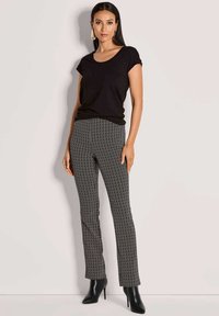 Zwarte korte mouwen shirt gecombineerd met slim-fit broek met een wit zigzagpatroon, afgemaakt met zwarte enkellaarsjes met hak.