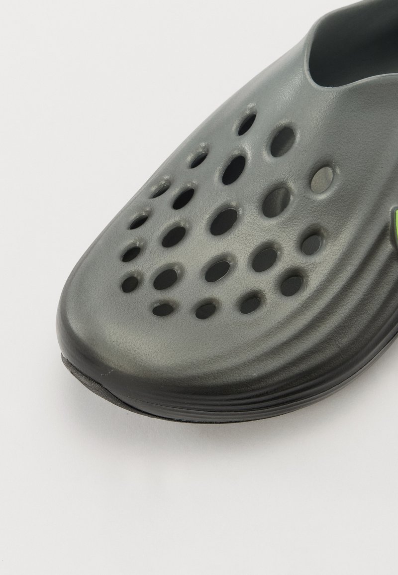 Botte grise à enfiler avec un bout arrondi, fabriquée dans un matériau semblable au caoutchouc. Dispose de plusieurs trous de ventilation et d'une texture lisse.