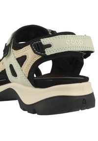 Sandale légère avec une base en maille noire, des accents crème et vert pâle, des sangles ajustables et une semelle rembourrée avec une texture antidérapante.