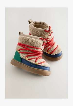 Bottes pour enfants en matériau beige et duveteux, avec des lacets rouges, des accents bleus et verts, une semelle en caoutchouc et un col rembourré pour le confort.