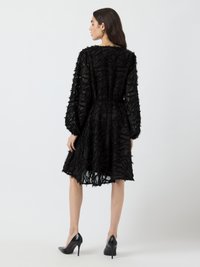 Black dress with a textured, layered design, long sleeves, and a cinched waist. Smooth fabric with a knee-length skirt. High-heeled shoes.