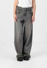 Jeans din denim gri cu croi larg prezintă o potrivire relaxată, cinci buzunare, detalii de cusătură și sunt asortați cu încălțăminte neagră.