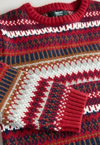 Gestrickter Pullover mit geripptem Kragen und Bündchen, der rote, marineblaue, weiße und braune geometrische und Zickzackmuster zeigt.