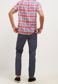 Koszula krótki rękaw w kratę w kolorach czerwonym, niebieskim i białym, zestawiona z granatowymi spodniami slim-fit i czarnymi butami, widziana z tyłu.