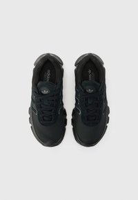 Chaussures de sport noires en matériaux mesh et suède, dotées d'une semelle épaisse, d'une surface texturée et de trois bandes réfléchissantes sur les côtés.