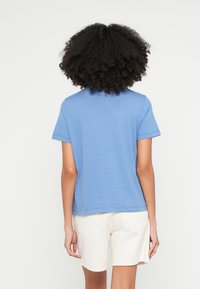 Kék, rövid ujjú, kerek nyakú póló, sima anyagból készült; világos színű rövidnadrággal viselve, tiszta és egyszerű kialakítást mutat.