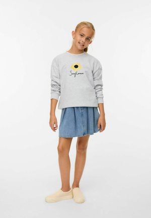 Light gray sweatshirt with a sunflower graphic, paired with a denim skirt and beige slip-on shoes. Smooth textures and relaxed fit.