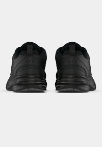 Par de ténis atléticos pretos visto de trás, com solas grossas e tiras para puxar na parte de trás do calcanhar.