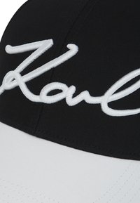 Czarny i biały kapelusz z wypukłym białym haftem na przednim panelu.