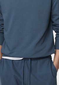Felpa blu scuro con maniche lunghe e polsini a costine, abbinata a pantaloni della tuta coordinati con vita regolabile tramite cordino e tasche laterali.