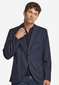 Marinblå blazer i strukturerad tyg, med en enkel knapp, slagkrage och två framfickor. Skräddarsydd passform med en avslappnad design.