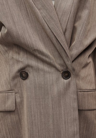 Καφέ διπλόσπαστο σακάκι με δύο σκούρα κουμπιά, πέτο με σχισμή και τσέπες με καπάκι, κατασκευασμένο από υφασμένο ύφασμα.