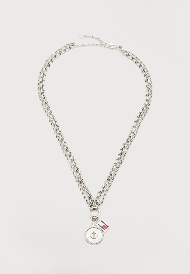 Διπλό ασημένιο κολιέ με αλυσίδα και μενταγιόν νόμισμα άγκυρα, καθώς και μικρό παραλληλόγραμμο γούρι με κόκκινη, λευκή και μπλε σημαία.