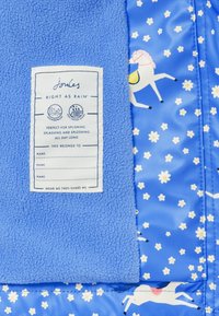 Blaues Fleece-Gewebe mit einem Etikett, das "Joules Right As Rain" liest, neben blauem Stoff mit einem Muster aus weißen Pferden und gelben Gänseblümchen.