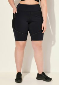 Zwarte high-waisted fietsbroek met een slank ontwerp, voorzien van mesh-accenten en geperforeerde details aan de zijkanten, gemaakt van rekbare stof.