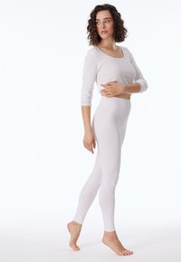 Haut blanc à manches longues et leggings ajustés, fabriqués en tissu doux, avec une texture lisse et un design simple sans coutures. Pieds nus.