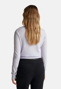 Jasnofioletowy sweter z długimi rękawami i prążkowanymi mankietami, zestawiony z czarnymi spodniami. Miękka tekstura i okrągły dekolt, minimalne detale na plecach.