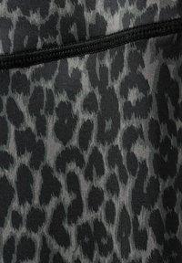 Tissu en imprimé léopard noir et gris avec une surface texturée, présentant un motif lisse de taches de tailles variées. Couture le long du bord supérieur.