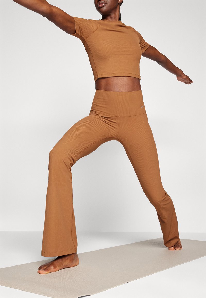 Top corto a coste marrone e pantaloni a palazzo aderenti abbinati, realizzati in tessuto elastico, indossati in una postura yoga su un tappetino.