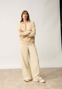 Pull en tricot beige avec un col et un pantalon large en crème à côtes. Tissu légèrement texturé et coupe décontractée, associé à des chaussures de sport.