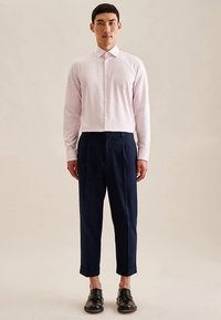 Camicia a righe bianche e rosa chiaro con bottoni, abbinata a pantaloni blu navy a gamba stretta. Scarpe nere in pelle completano l'outfit.