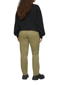 Zwart oversized trui gecombineerd met olijfgroene katoenen broek. De broek heeft twee achterzakken en is tapered bij de enkels. Zwarte chunky schoenen.