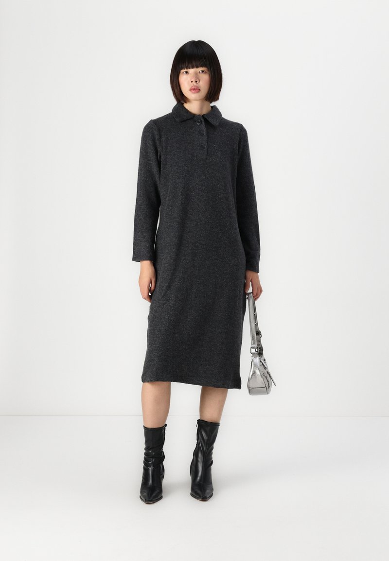 Robe polo grise à manches longues avec un col boutonné, fabriquée en tissu doux. Portée avec des bottines noires et un sac à épaule argenté.