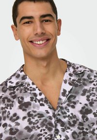 Camisa de manga corta en material sedoso con un estampado abstracto en negro y gris, que presenta un cuello puntiagudo y cierre de botones.