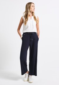 Marineblauwe wijde broek van een lichte stof, met een elastische taille trekkoord en zijzakken, gecombineerd met een wit mouwloos top.