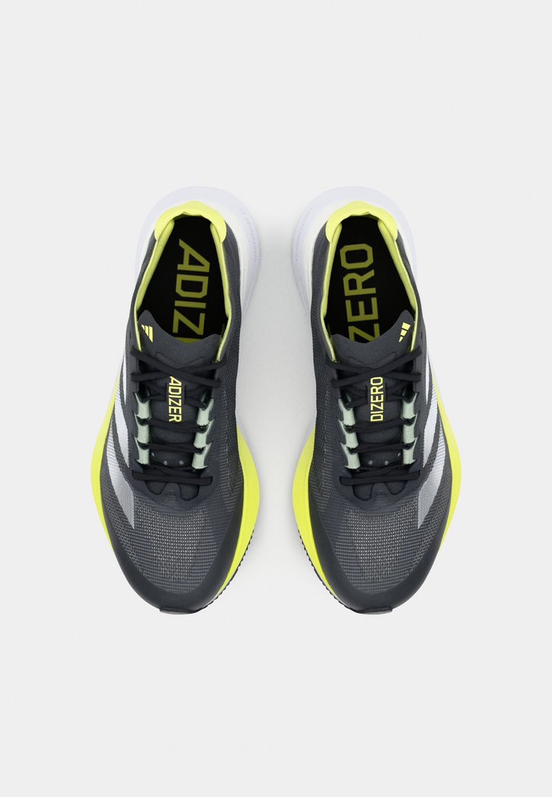 Czarne i żółte buty sportowe z siateczkową cholewką, o smukłym kształcie, z teksturowanymi wzorami, jasnopomarańczowymi akcentami i białą podeszwą.