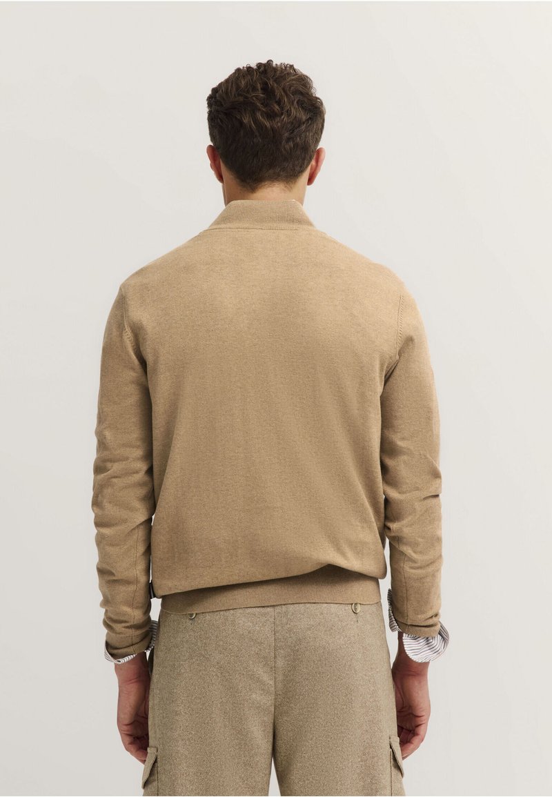 Maglione beige con colletto e polsini a costine, caratterizzato da una texture liscia e una vestibilità casual. Lo sfondo è neutro e discreto.