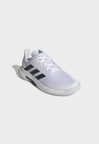 White athletic shoe with synthetic mesh upper, featuring three black stripes, textured design, and a rounded rubber sole.