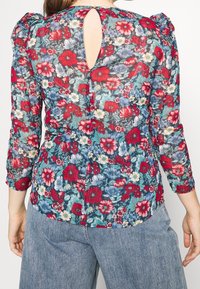 Floral blouse featuring a sheer blue fabric with red, pink, and white flowers. Back keyhole detail and puffed sleeves. Textured appearance.