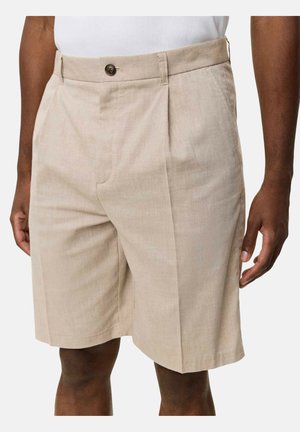 Pantaloncini beige su misura con pieghe frontali, chiusura con bottoni e tasche laterali indossati da una persona con pelle scura e top bianco.