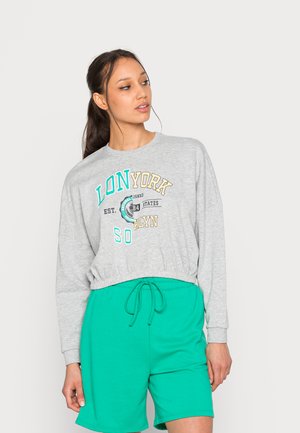 Sweatshirt court gris avec texte graphique, associé à un short vert à cordon. Les deux sont fabriqués dans des matériaux doux et légers.